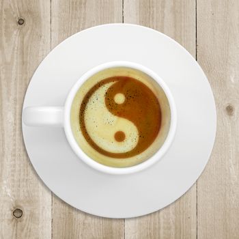 Cup of coffee standing on a wooden surface. Picture of the yin-yang in the coffee crema. top view