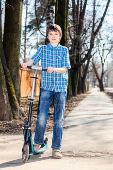 Cute boy standing with his push scooter outdoors