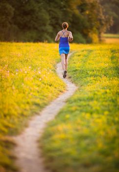 Young woman running outdoors on a lovely sunny summer evening (shallow DOF; color toned image)