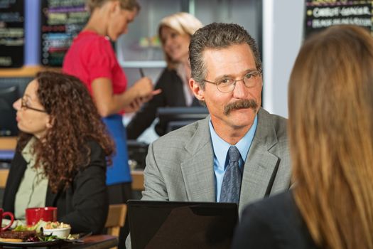 Executive with mustache listening to woman in cafe