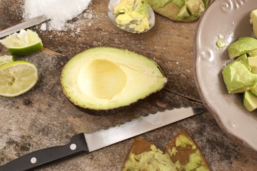 Preparing a delicious healthy avocado salad on an old rustic wooden countertop with a halved avocado pear, lemon and salt to prevent discoloration of the sliced fruit