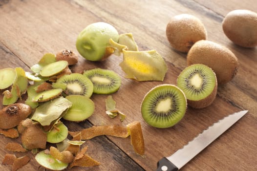 Peeling and slicing fresh tropical kiwifruit for dessert with whole and halved fruit and peels lying on a wooden kitchen counter with a knife