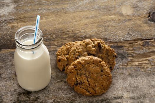 Milk and cookies childhood treat set out on an old rustic wooden table with a glass bottle of fresh milk with a straw and a pile of crunchy cookies, high angle with copyspace