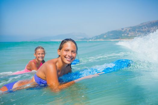 Summer vacation - Happy cute girls having fun with surfboard in the ocean