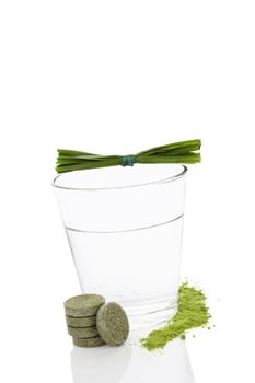 Green effervescent pills, green powder and glass of water isolated on white background. Chlorella, spirulina, wheat grass and barley grass. Healthy natural herbal medicine, healthy lifestyle.