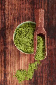 Green food supplement. Wheatgrass ground on brown wooden scoop and round bowl on brown wooden background, top view. Healthy natural detox. 