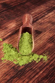 Green food supplement. Wheatgrass ground on brown wooden scoop on brown wooden background. Healthy natural detox. 