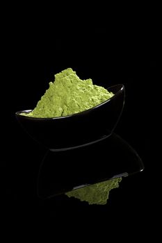 Green nutritional food supplement. Green ground wheatgrass powder isolated on black background.