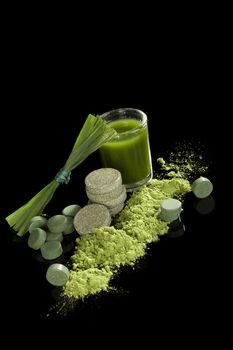 Green nutritional food supplement. Green pills, grass blades, effervescent tablets and green juice isolated on black background. Natural detox. 