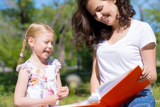 girl with the teacher reading a book together in the summer park