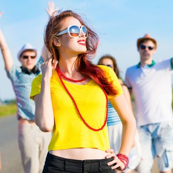 stylish young woman in sunglasses on the background of blue sky and friends