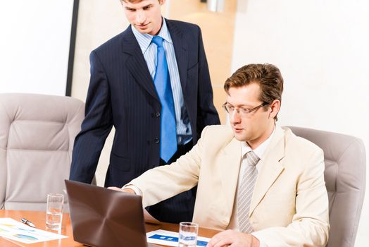 Business people talking, sitting at the table, watching the presentation on a laptop