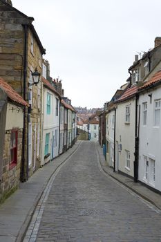 View along the length of the narrow cobbled Henrietta Street, Whitby, North Yorkshire with its traditional historical English cottages