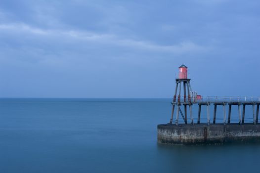 Whitby pier with one of the navigation beacons to guide shipping into the harbour at night on a calm ocean with copyspace