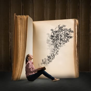 image of a young woman reading a book sitting near a big book