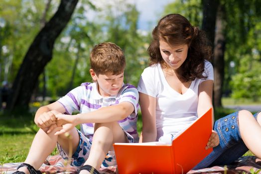 boy and a woman in a summer park reading a book together