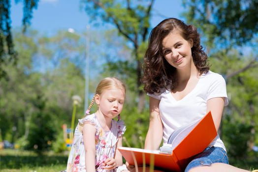 girl with the teacher reading a book together in the summer park