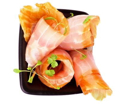 Snack of Swirled Slices of Delicious Smoked Sturgeon with Greens in Black Bowl isolated on white background. Top View