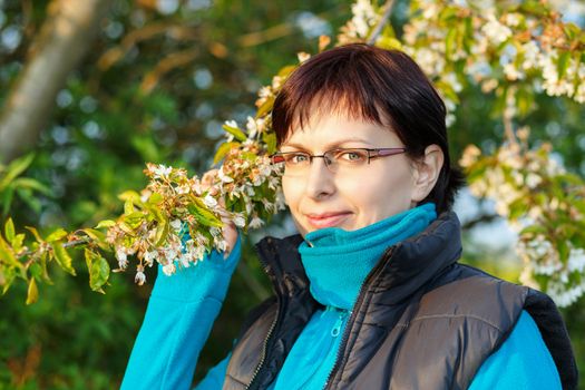 happy smiling middle age woman without makeup outdoor with flowering cherry tree in evening sun