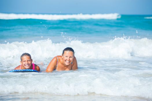 Summer vacation - Happy cute girl and her mother having fun with surfboard in the ocean
