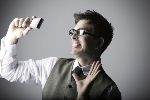 Laughing young man makes a selfie with a compact camera against grey background