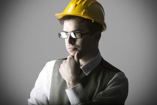 Portrait of thoughtful smart young engineer with helmet against grey background