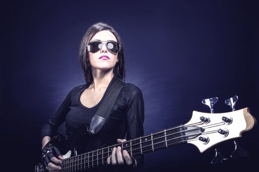 Young brunette woman playing bass against dark blue background, Music concept portrait