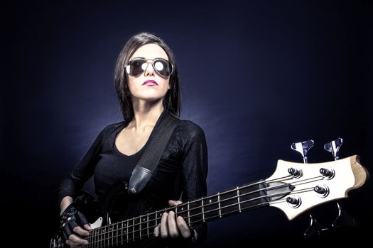 Young brunette woman playing bass against dark blue background, Music concept portrait