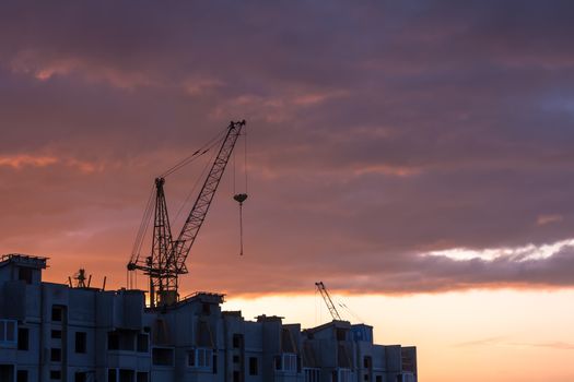 Silhouette of construction crane on dramatic sky background at the sundown