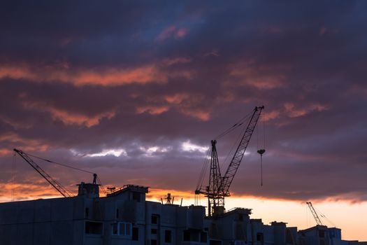 Silhouette of construction crane on dramatic sky background at the sundown