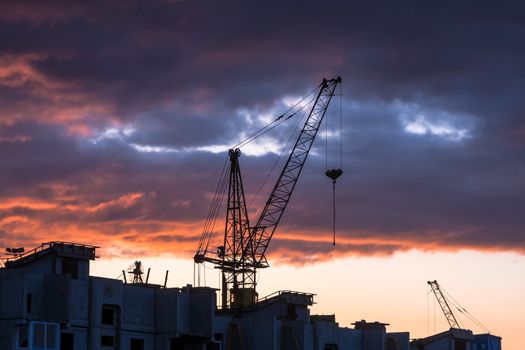Silhouette of construction crane on dramatic sky background at the sundown