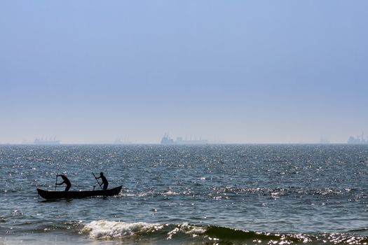 Boat with fishermans at Arabian sea. Cargo ship on the background