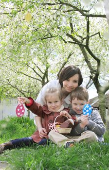 Happy mother and two children in blooming garden with Easter eggs