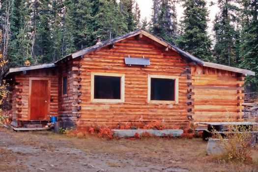 Old weathered traditional Yukon log cabin with exterior off-grid solar panel in the boreal forest taiga of Yukon Territory, Canada