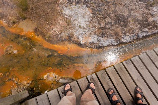 Feet on wooden boardwalk over geothermal hot water in Orakei Korako geothermal wonderland just south of Rotorua, North Island of New Zealand