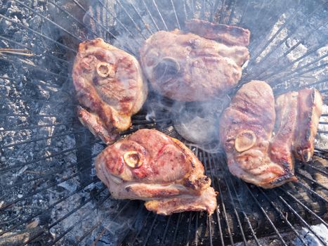 Crispy brown pork meat steaks grill over hot coals of bbq wood fire on metal grate grid