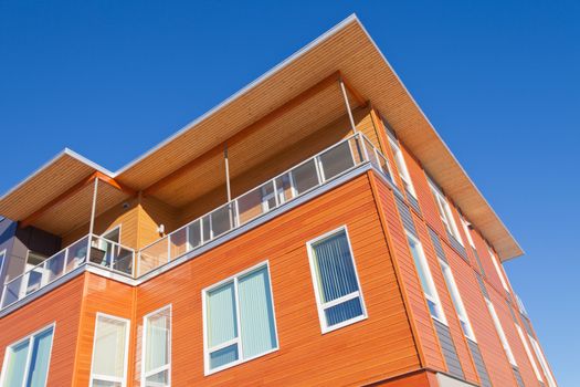 Upper storey detail of timber clad apartment building painted bright with penthouse balcony under blue sky