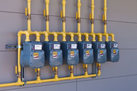 Row of residential natural gas meters and yellow pipe plumbing on exterior wall to measure household energy consumption