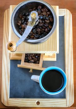Cup of coffee, brewed with beans and a coffee grinder on the balckboard background