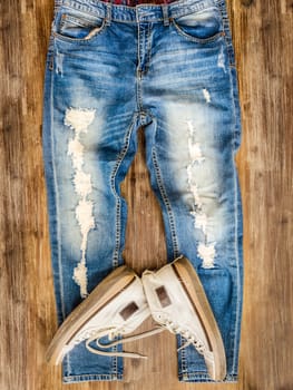 Detail of vintage weathered jeans and old shoes on wood texture