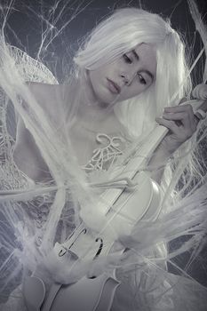 Sexy beautiful woman trapped in a spider web with a white violin, lace dress