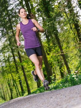 Photo of a young woman jogging and exercising on a gravel path through a forest. Slight motion blur on jogger.