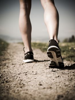Photo of the legs and shoes of a young woman jogging on a gravel path down a country path. Heavily filtered for atmosphere.
