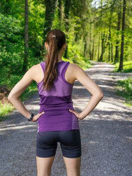 Photo of a young woman looking down the gravel path through a forest before she starts her exercise.