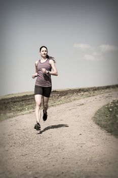 Photo of a beautiful young woman running down a gravel road. 
