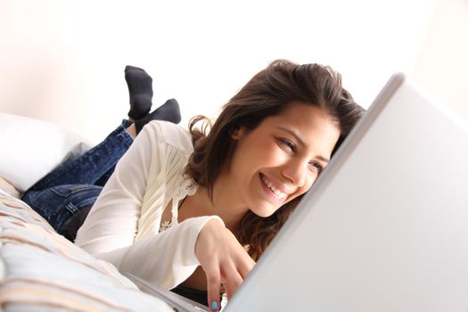 A young girl laying on the bed and surfing on the Internet with a Laptop.  
