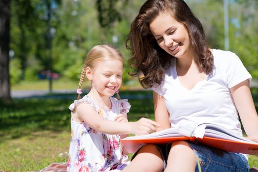 girl with the teacher reading a book together in the summer park