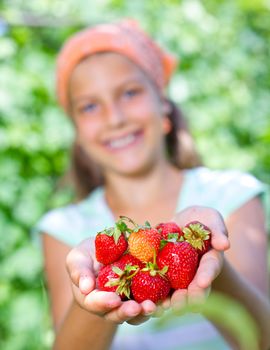 Happy cute girl in summer garden with ripe fresh strawberries. Focus on the strawberries.