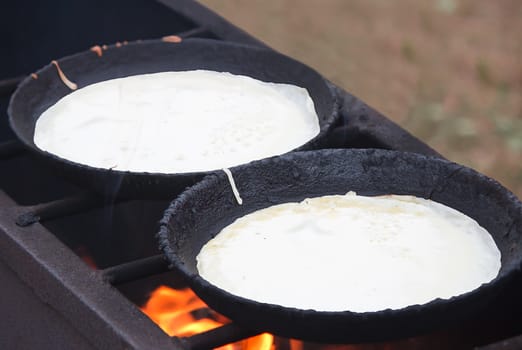 Two big frying pans in which on a grill pancakes are fried