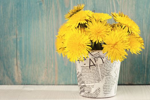 Dandelions in a news paper pot on a white blue wooden background 